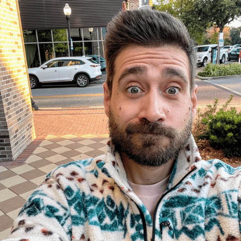 Close-up of a man taking a selfie outdoors in front of Pensacola State College.