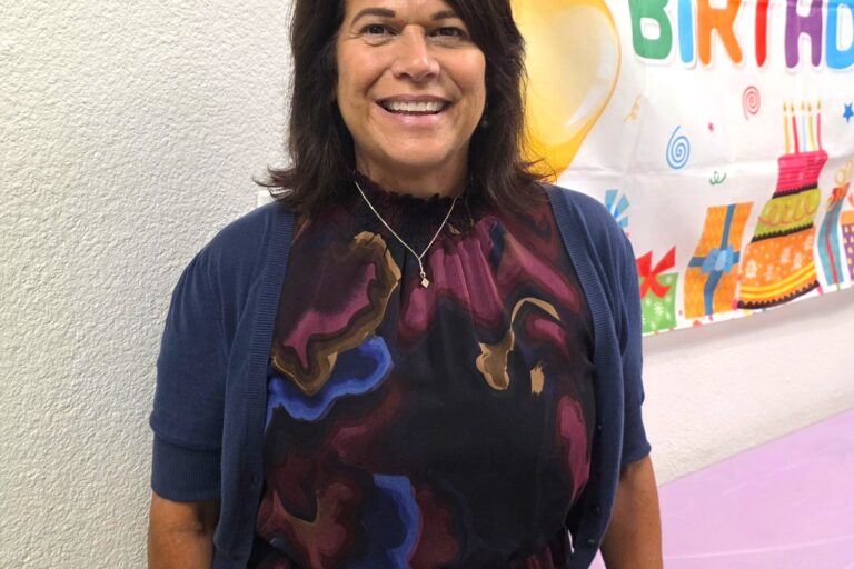 Woman smiling at birthday celebration with colorful decorations in background.