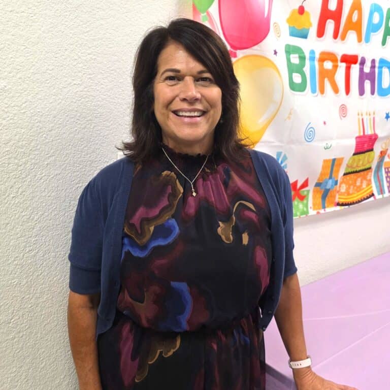 Woman smiling at birthday celebration with colorful decorations in background.