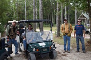 Group of men at a clay shooting event in a wooded outdoor setting.