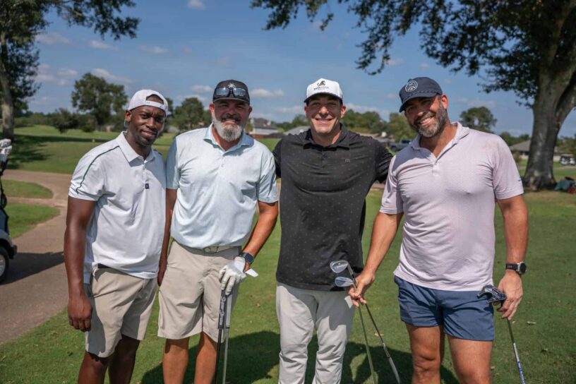 Byron Cobb, Chuck Crocco, Andrew Vose, and Billy Scarborough of Team Hole-In-Fun pose together on a golf course.