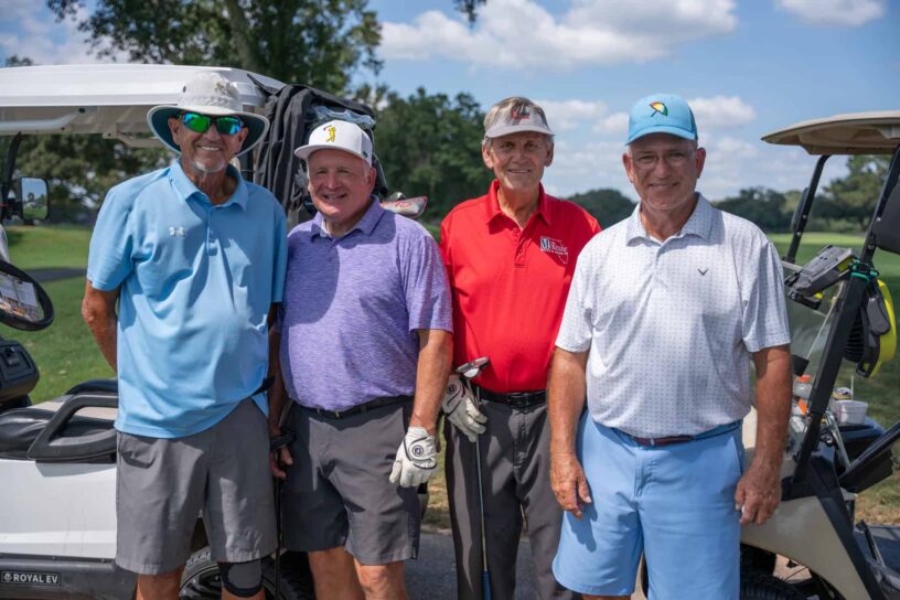 Bam Burch, Gregg Gullickson, Jim Windrow, and Gary Gilmore of Team McKenzie Buick-GMC pose together on a golf course.