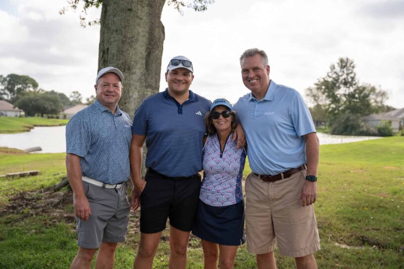 Todd Potter, Mike Flores, Karin Feagles, and David Gooch of Team PenAir Credit Union pose together on a golf course.